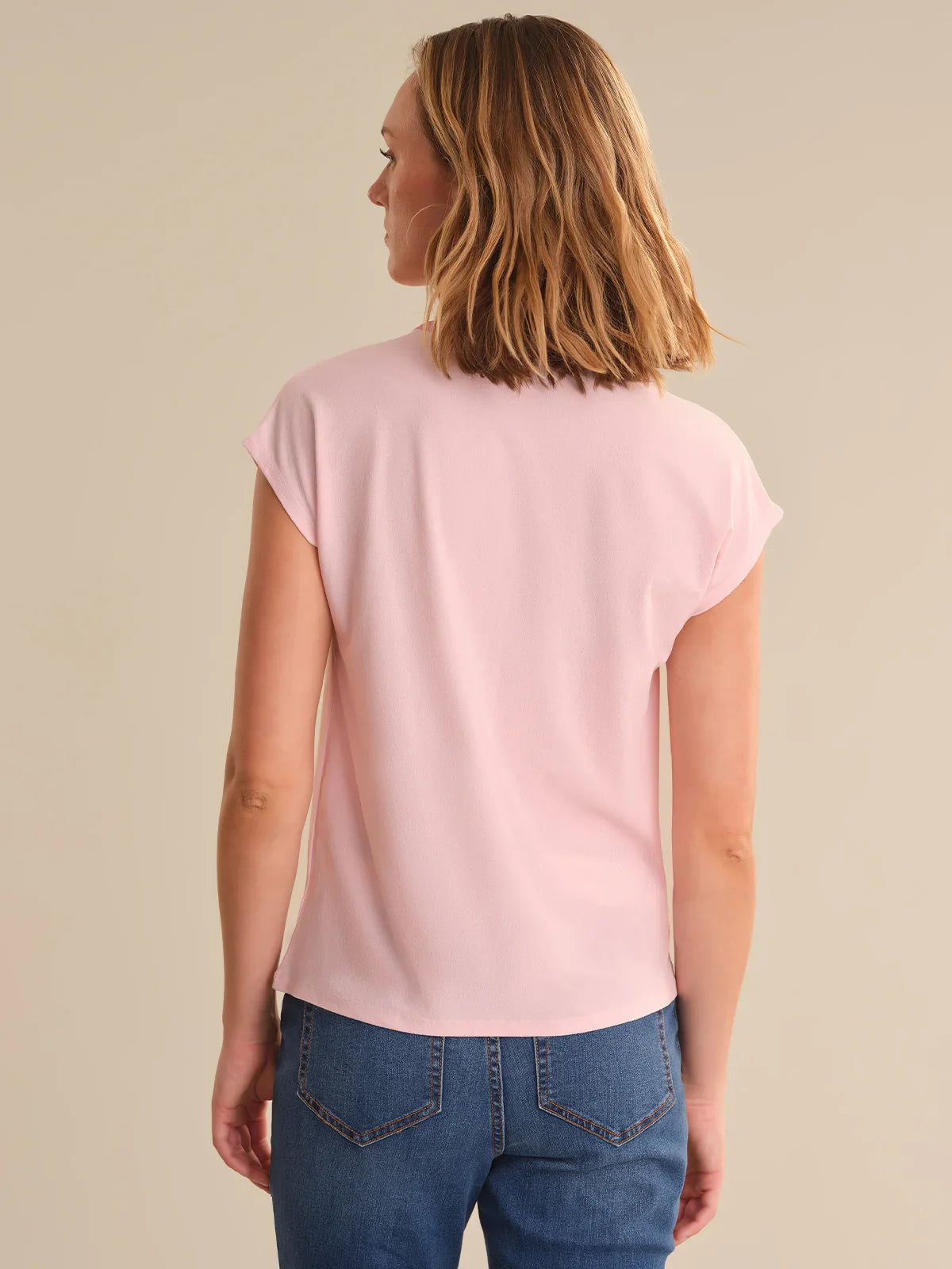 Woman wearing a pink t-shirt and blue jeans on a beige background