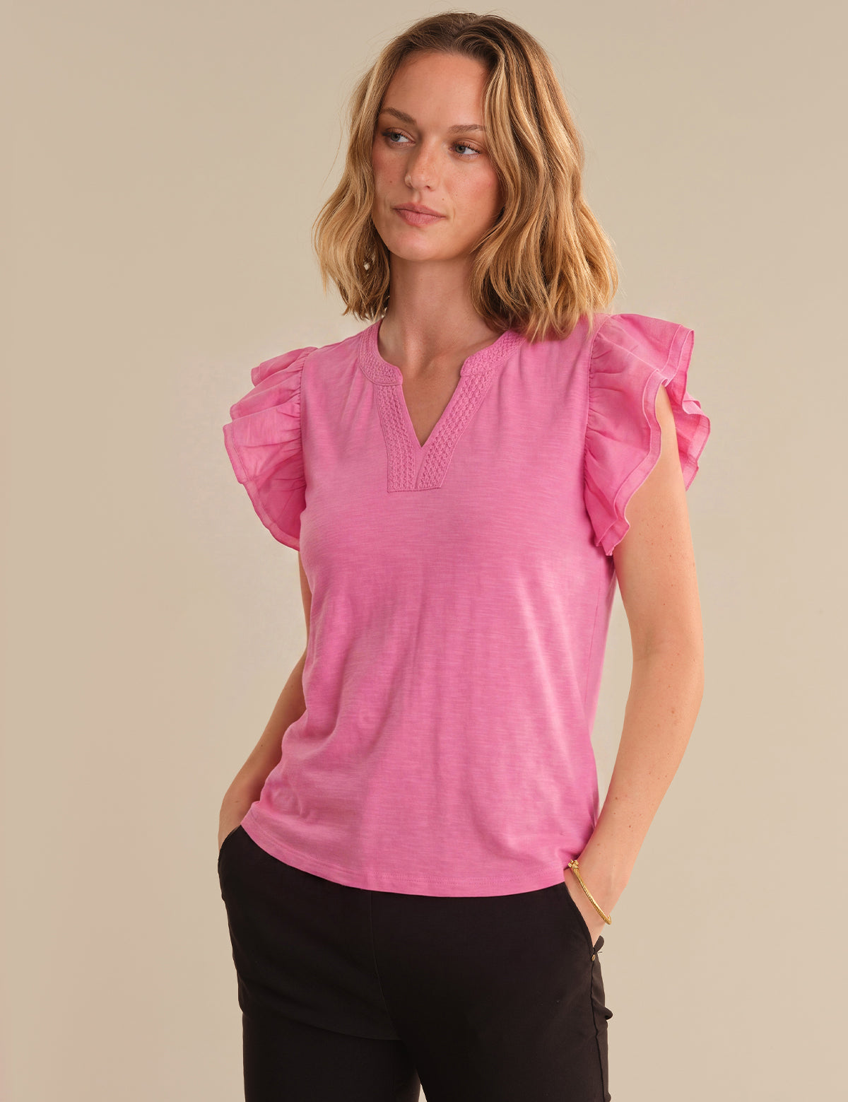 Woman wearing a pink blouse with ruffled sleeves against a beige background
