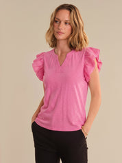 Woman wearing a pink blouse with ruffled sleeves against a beige background
