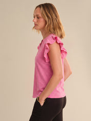 Woman wearing a pink top with ruffled sleeves against a beige background