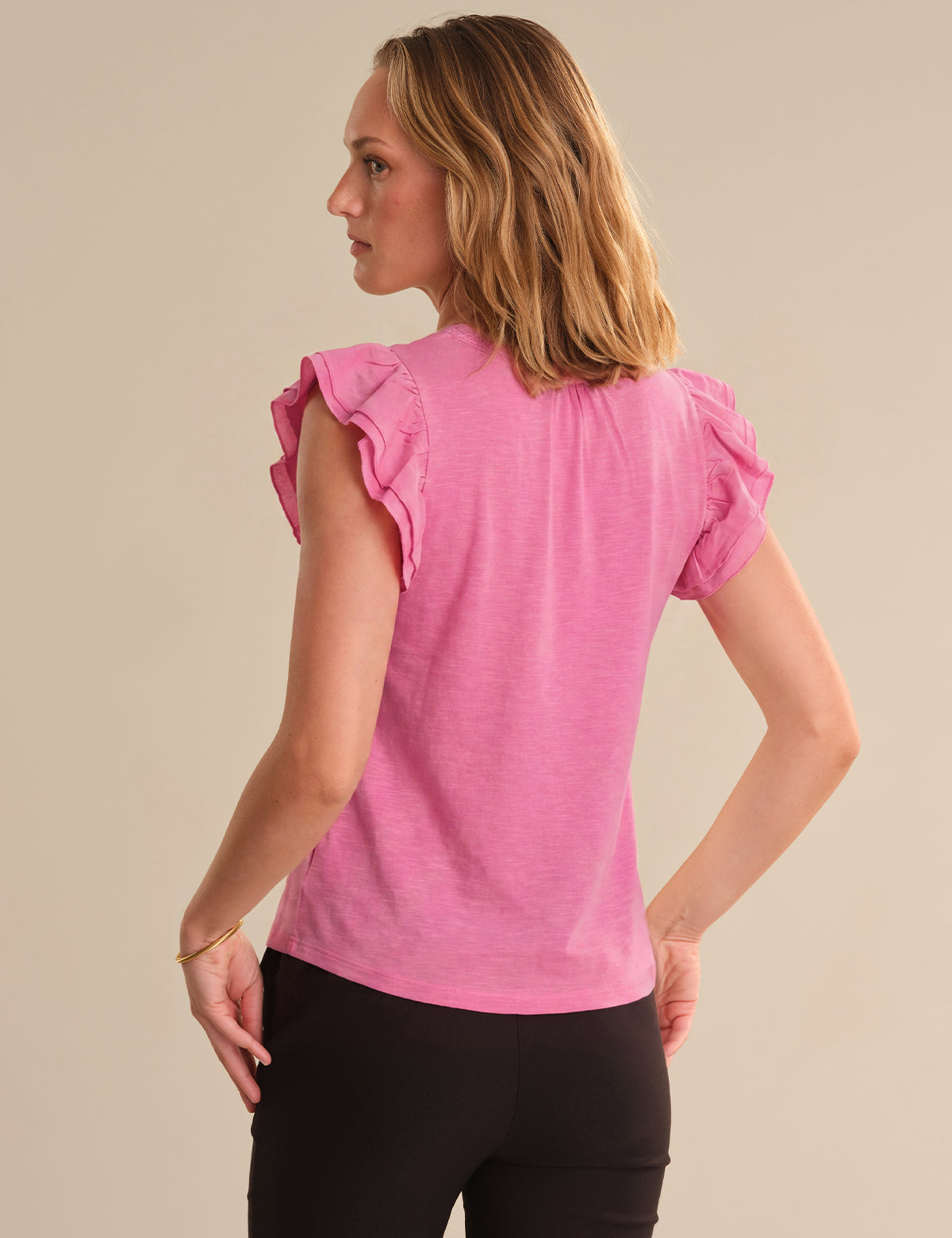 Woman wearing a pink top with ruffled sleeves on a beige background