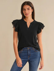 Woman wearing a black top with ruffled sleeves and blue jeans on a beige background