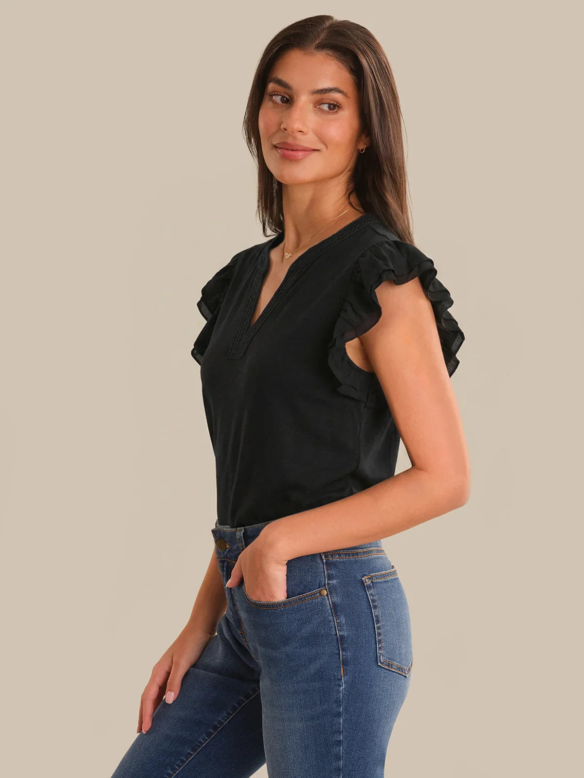 Woman wearing a black top with ruffled shoulders and blue jeans on a beige background