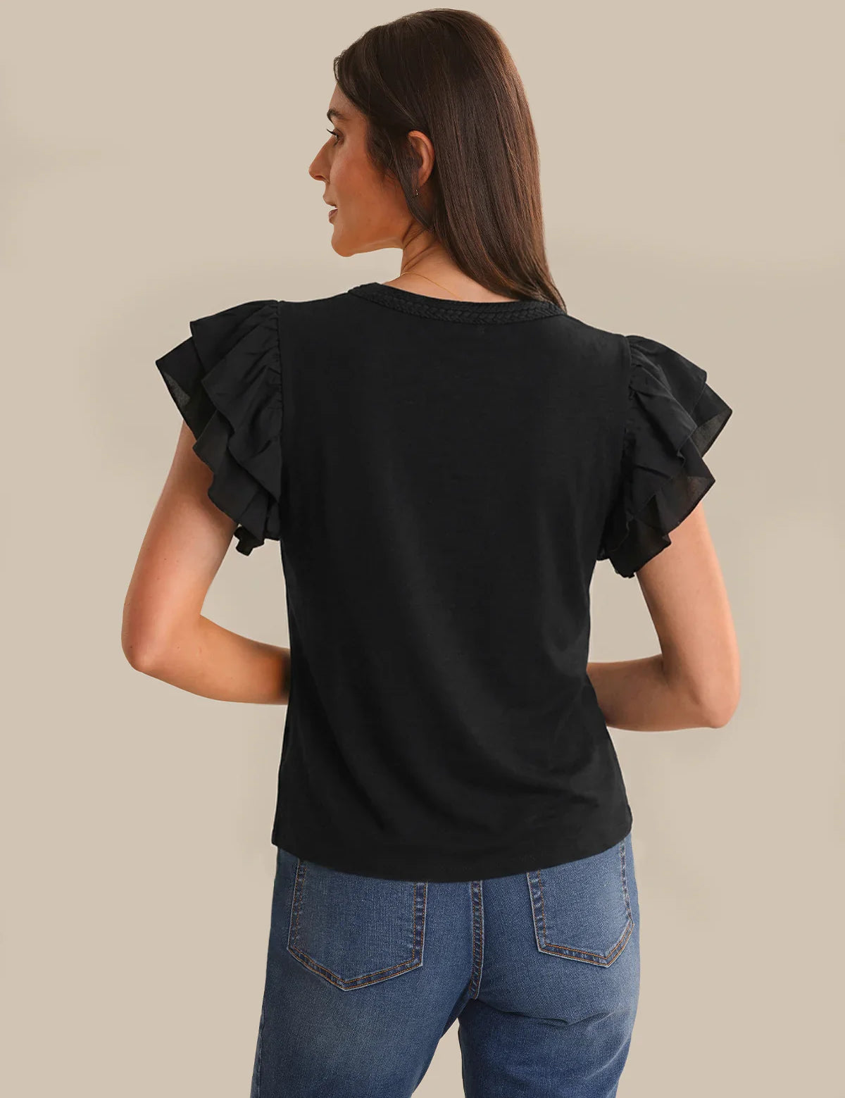 Woman wearing a black ruffled sleeve top and blue jeans on a beige background