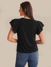 Woman wearing a black ruffled sleeve top and blue jeans on a beige background