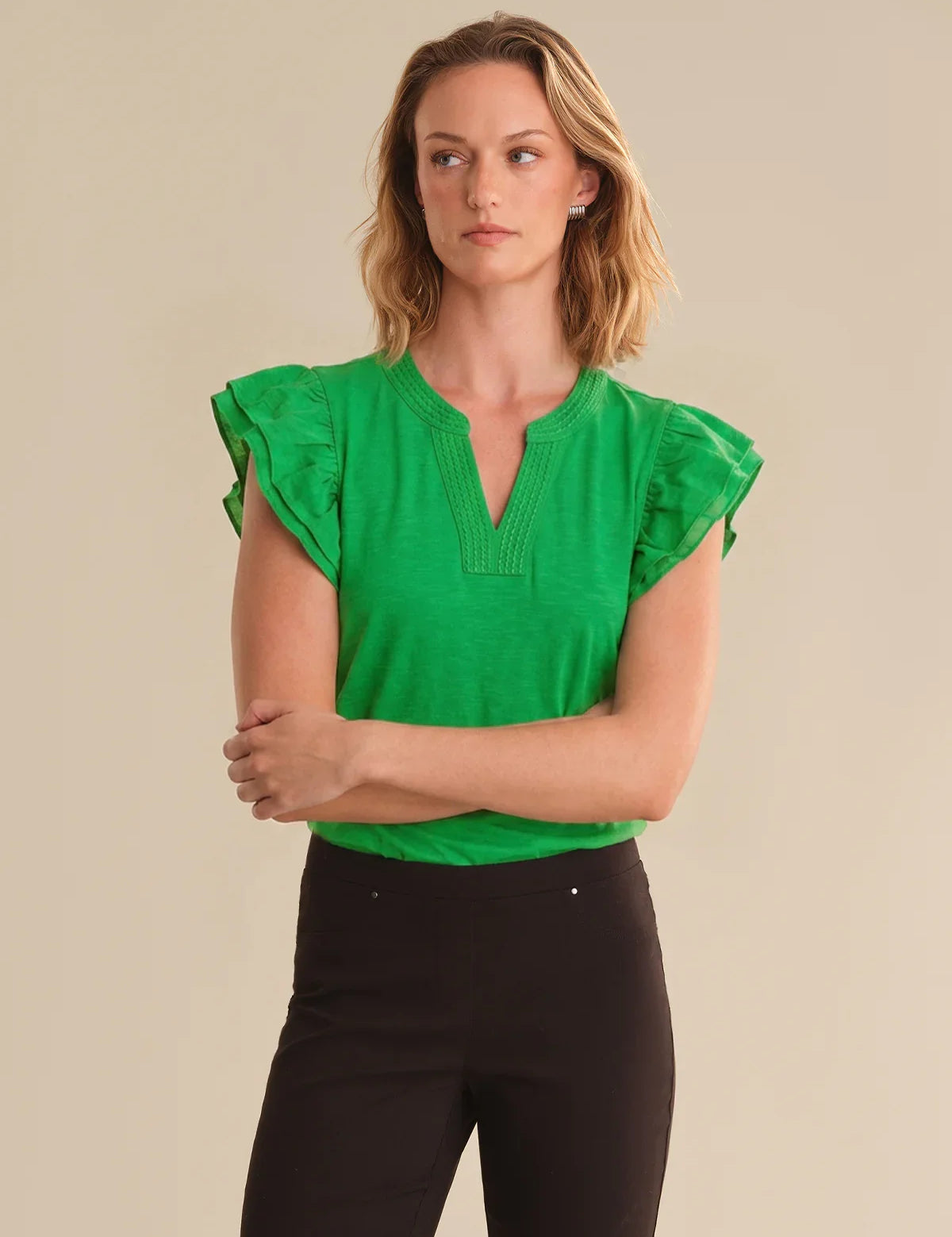 Woman wearing a green top with ruffled sleeves against a beige background