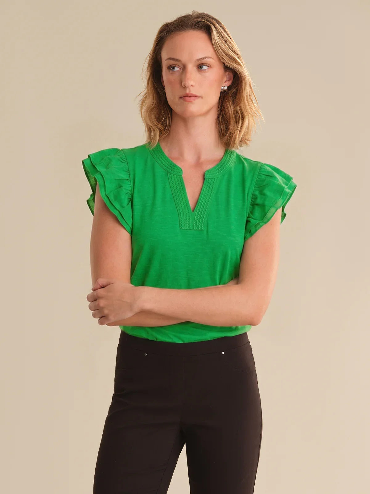 Woman wearing a green top with ruffled sleeves against a beige background