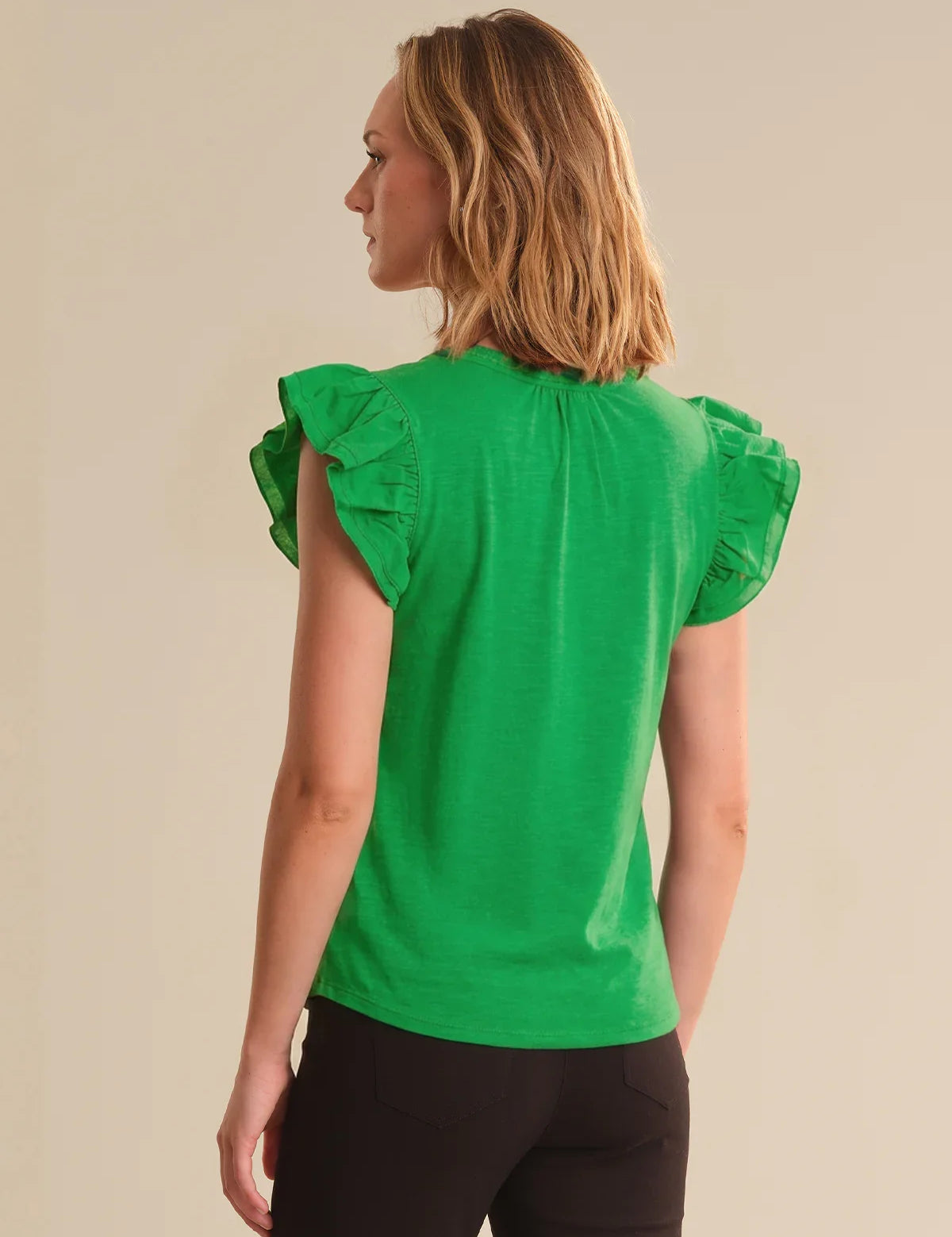 Woman wearing a green top with ruffled sleeves on a beige background