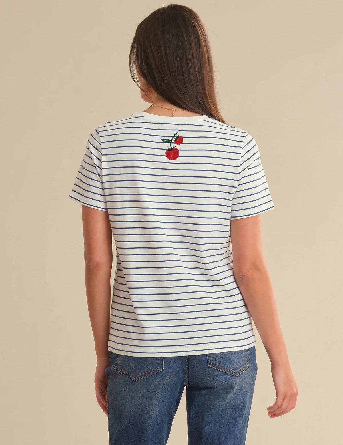 Person wearing a striped t-shirt with a tomato design on the back, standing against a beige background.