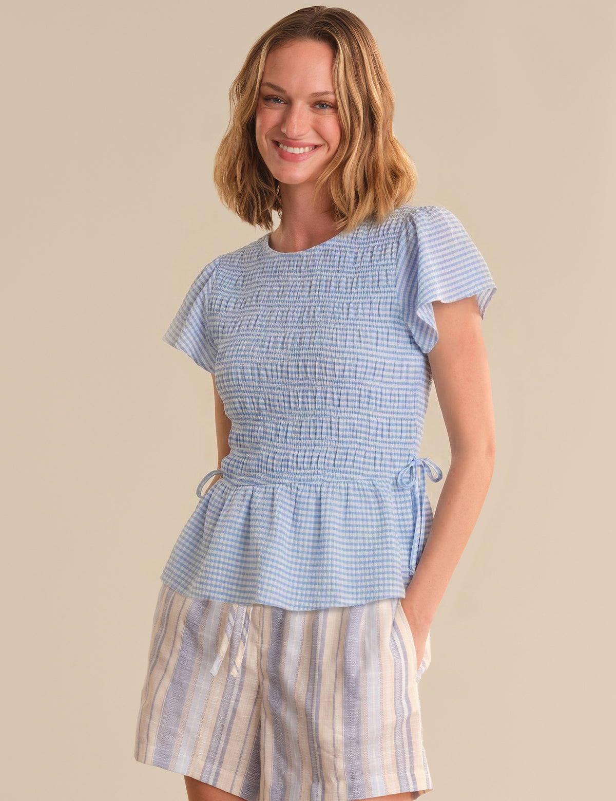 Woman wearing a blue checkered top and striped skirt on a beige background