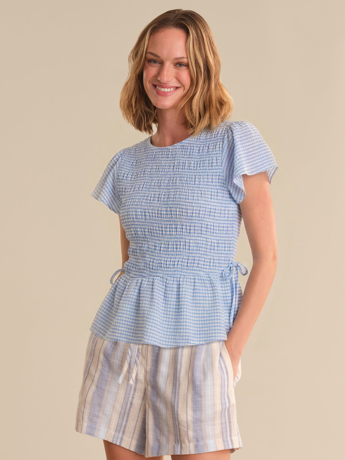 Woman wearing a blue checkered top and striped skirt on a beige background