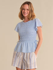 Woman wearing a blue checkered top and striped skirt on a beige background