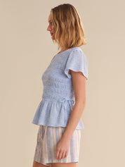 Woman wearing a blue checkered top and striped skirt on a beige background