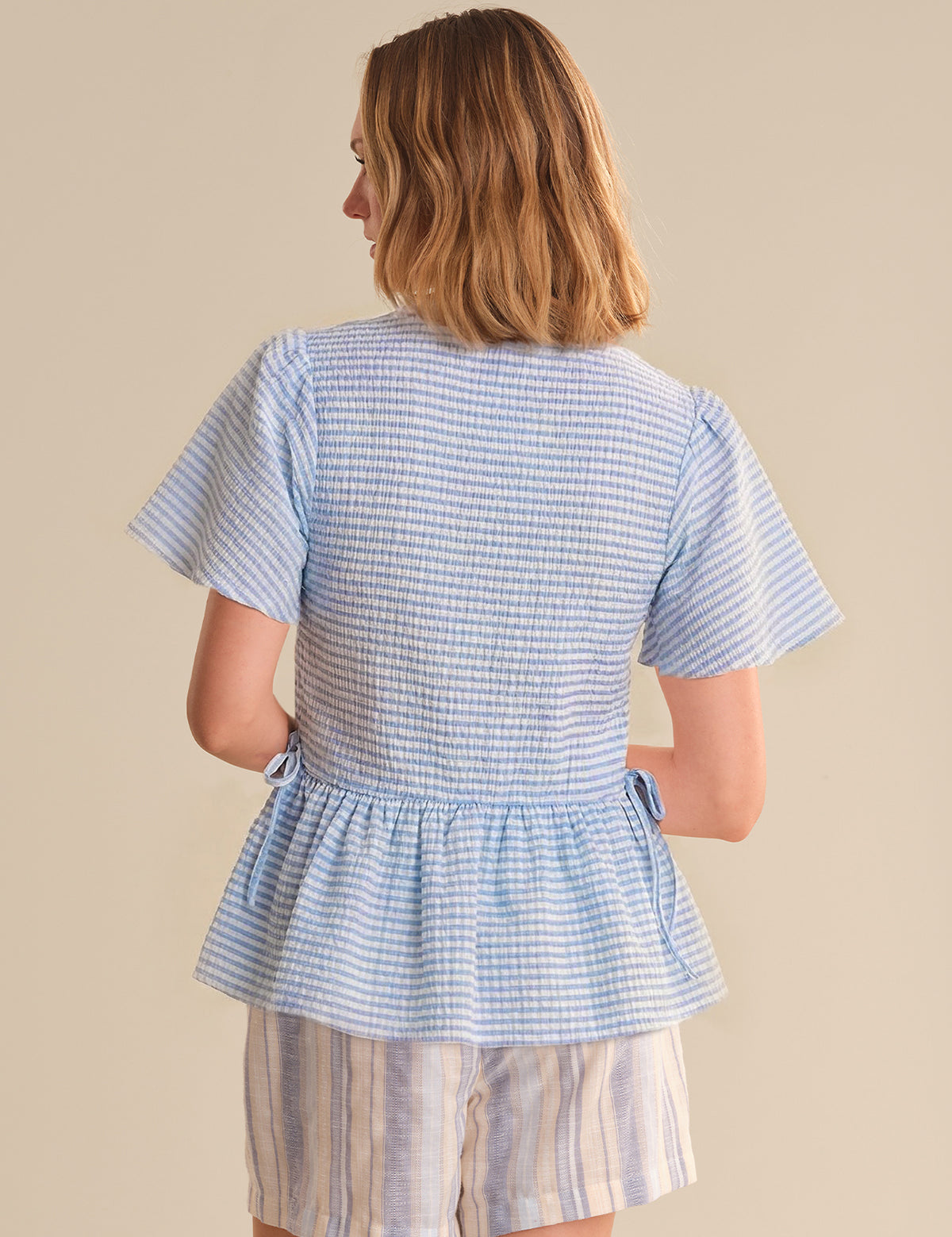 Woman wearing a blue checkered top and shorts on a beige background