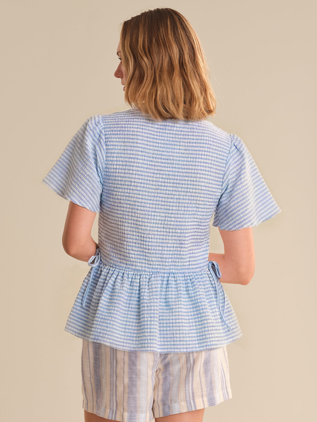 Woman wearing a blue checkered top and shorts on a beige background