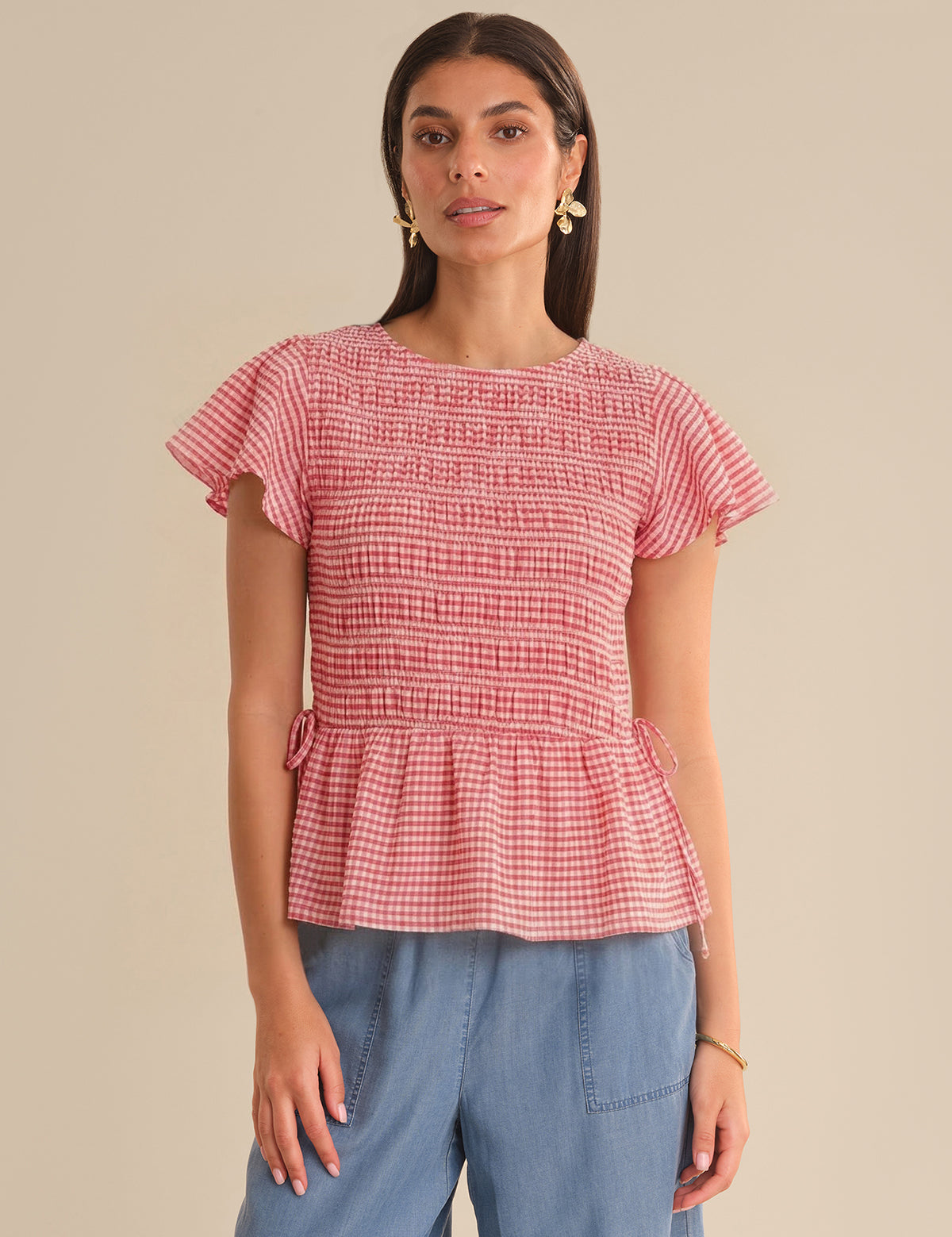 Woman wearing a red checkered top with ruffled details on a beige background