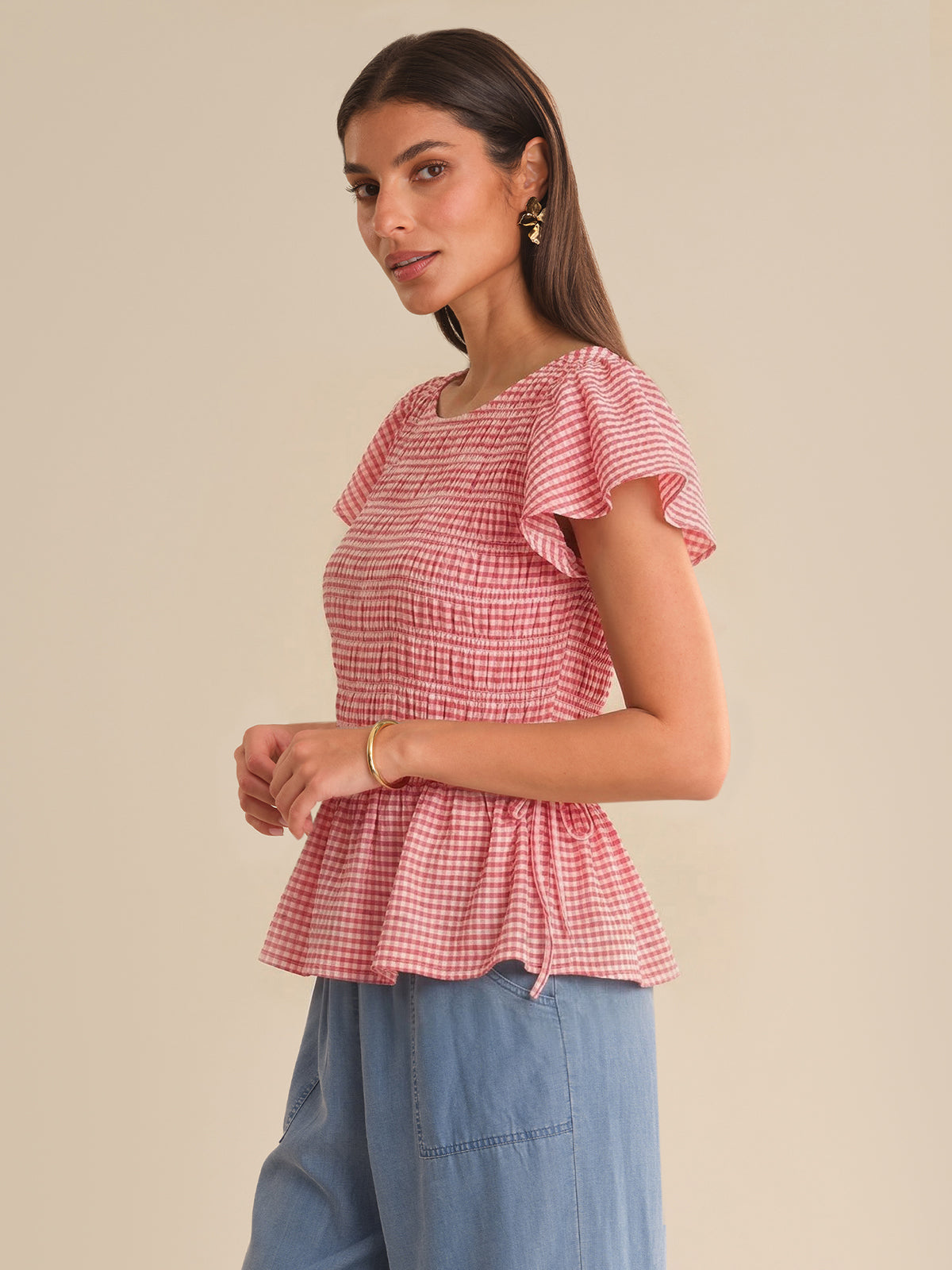 Woman wearing a red and white checkered top with ruffled sleeves on a beige background