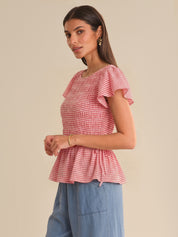 Woman wearing a red and white checkered top with ruffled sleeves on a beige background