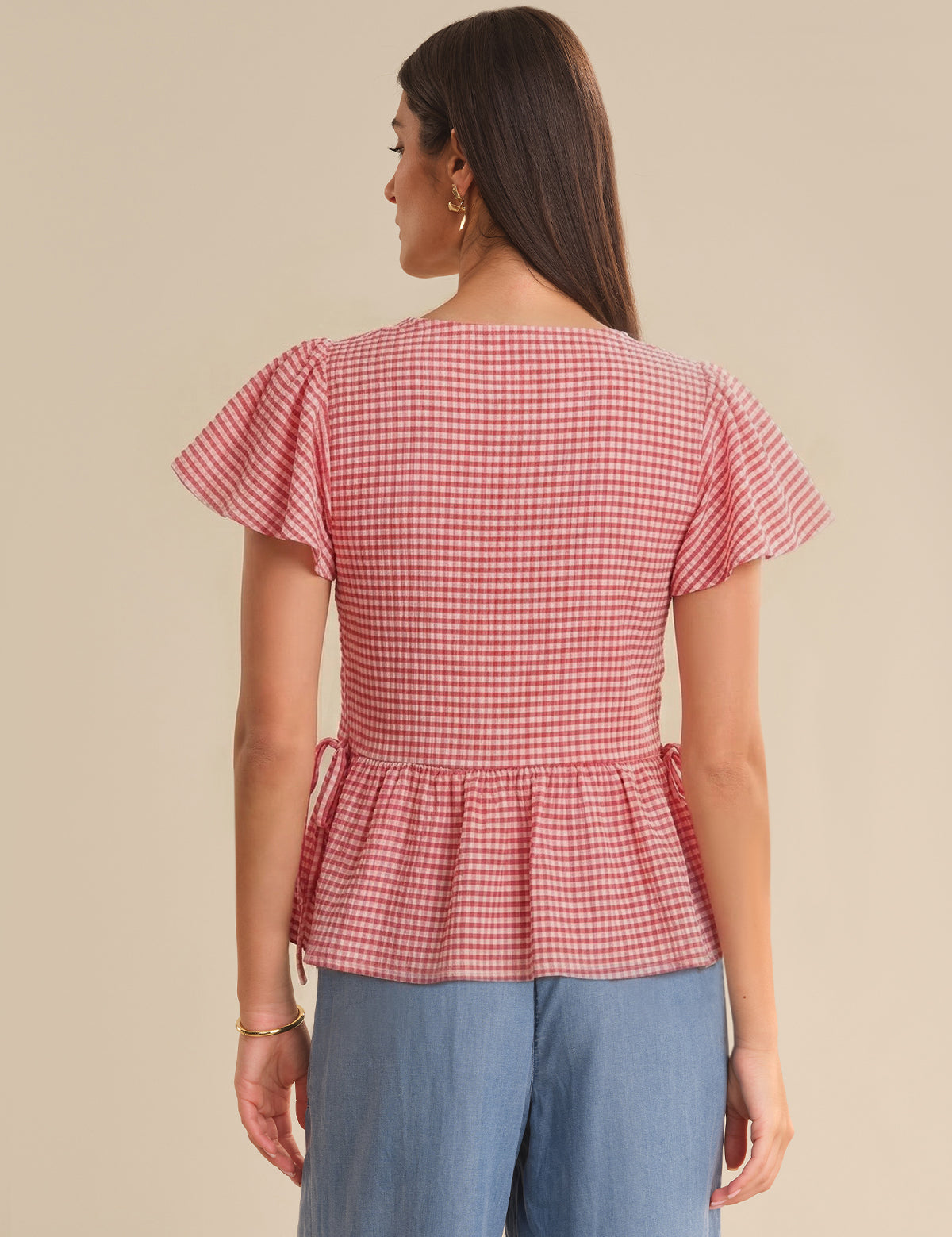 Woman wearing a red and white checkered top with ruffled sleeves on a beige background