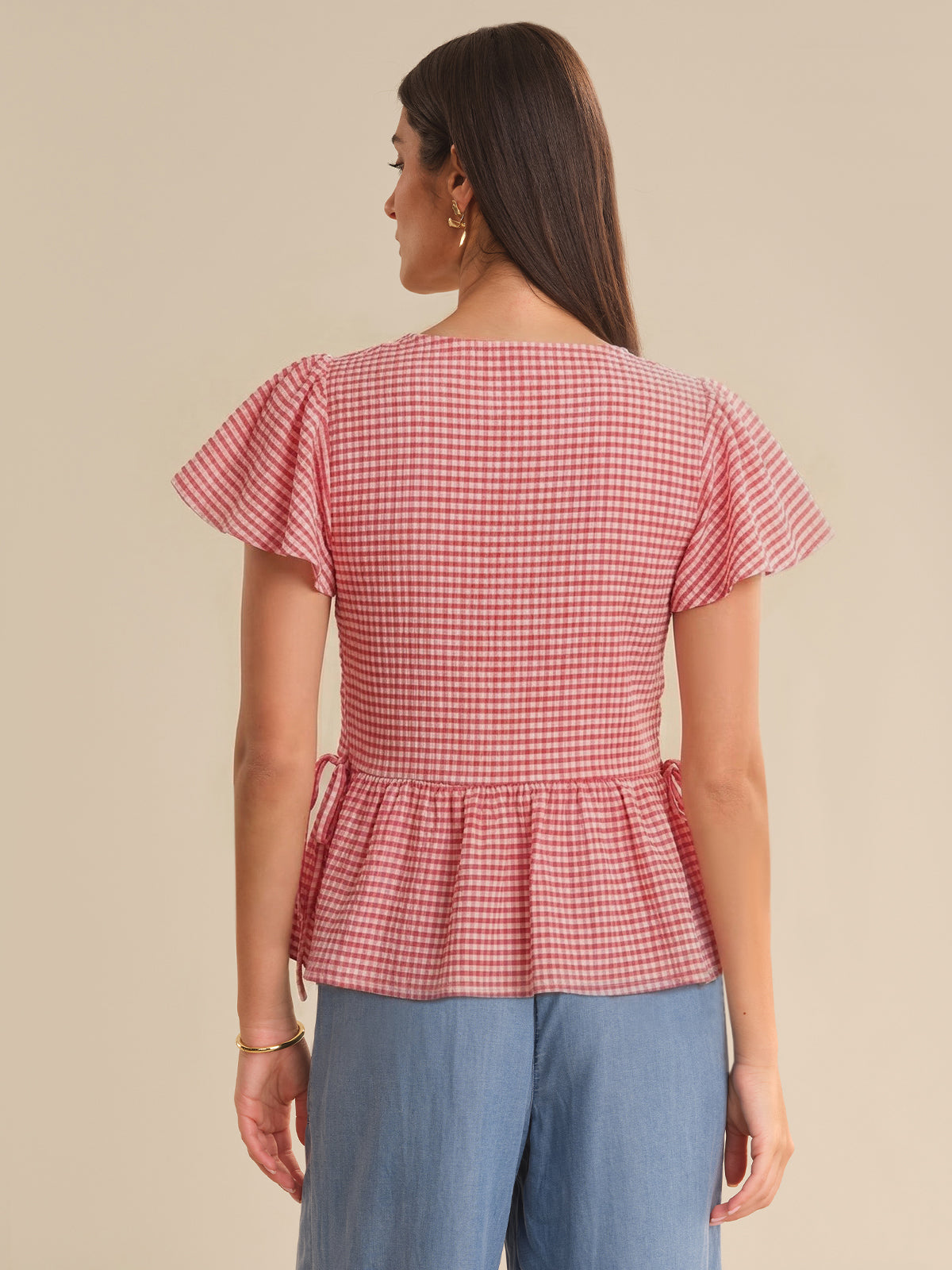 Woman wearing a red and white checkered top with ruffled sleeves on a beige background