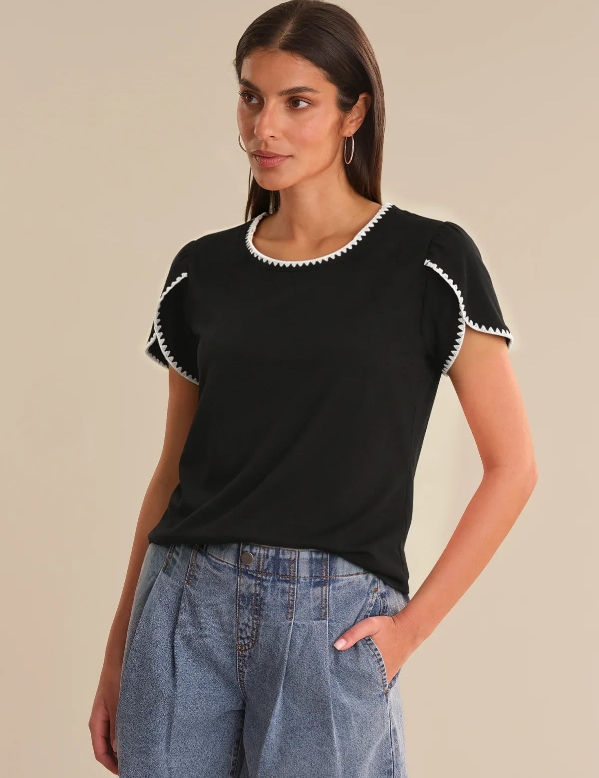 Woman wearing a black top with white trim and blue jeans on a beige background