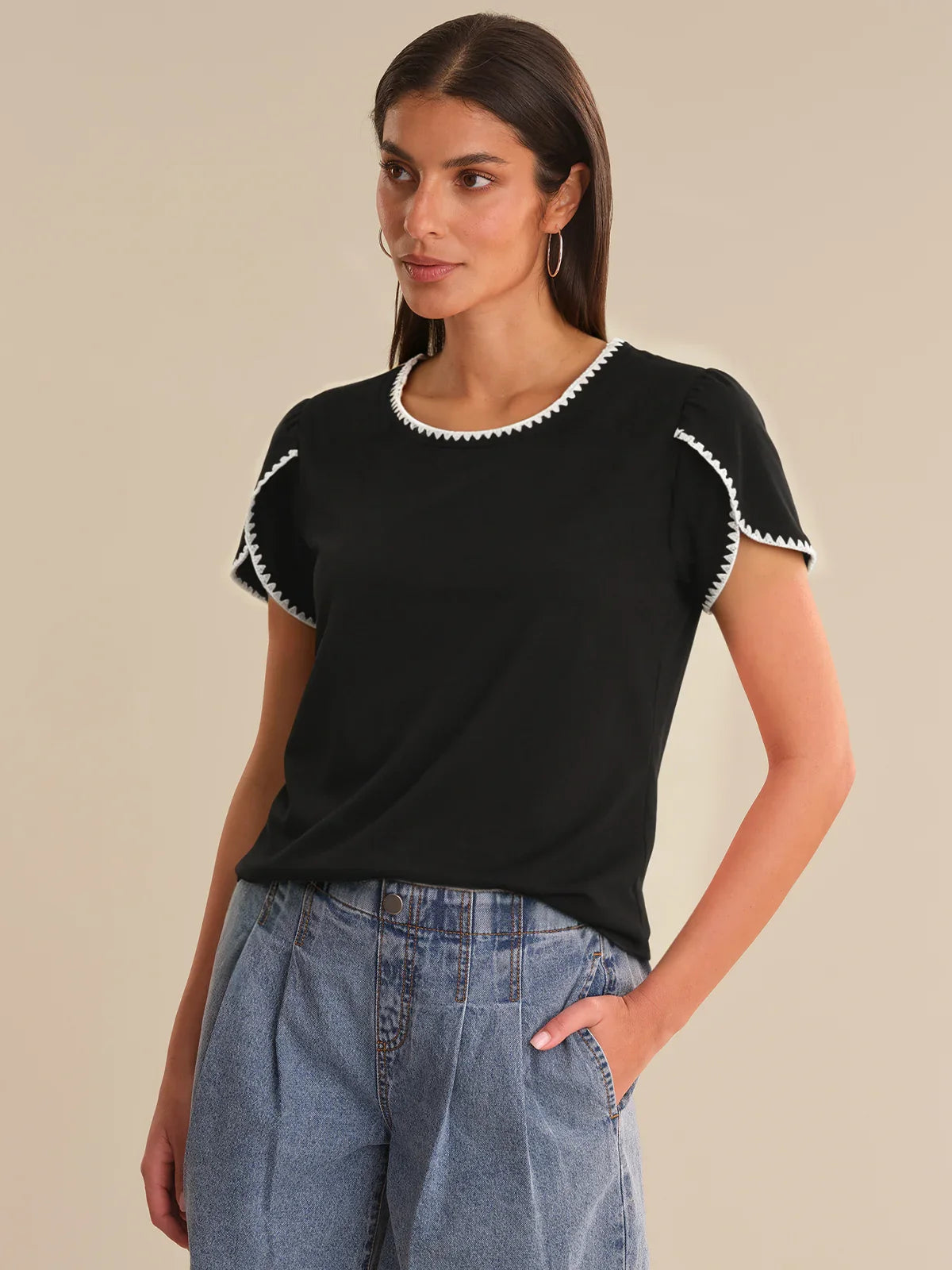Woman wearing a black top with white trim and blue jeans on a beige background
