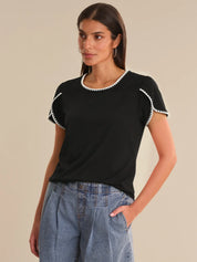 Woman wearing a black top with white trim and blue jeans on a beige background