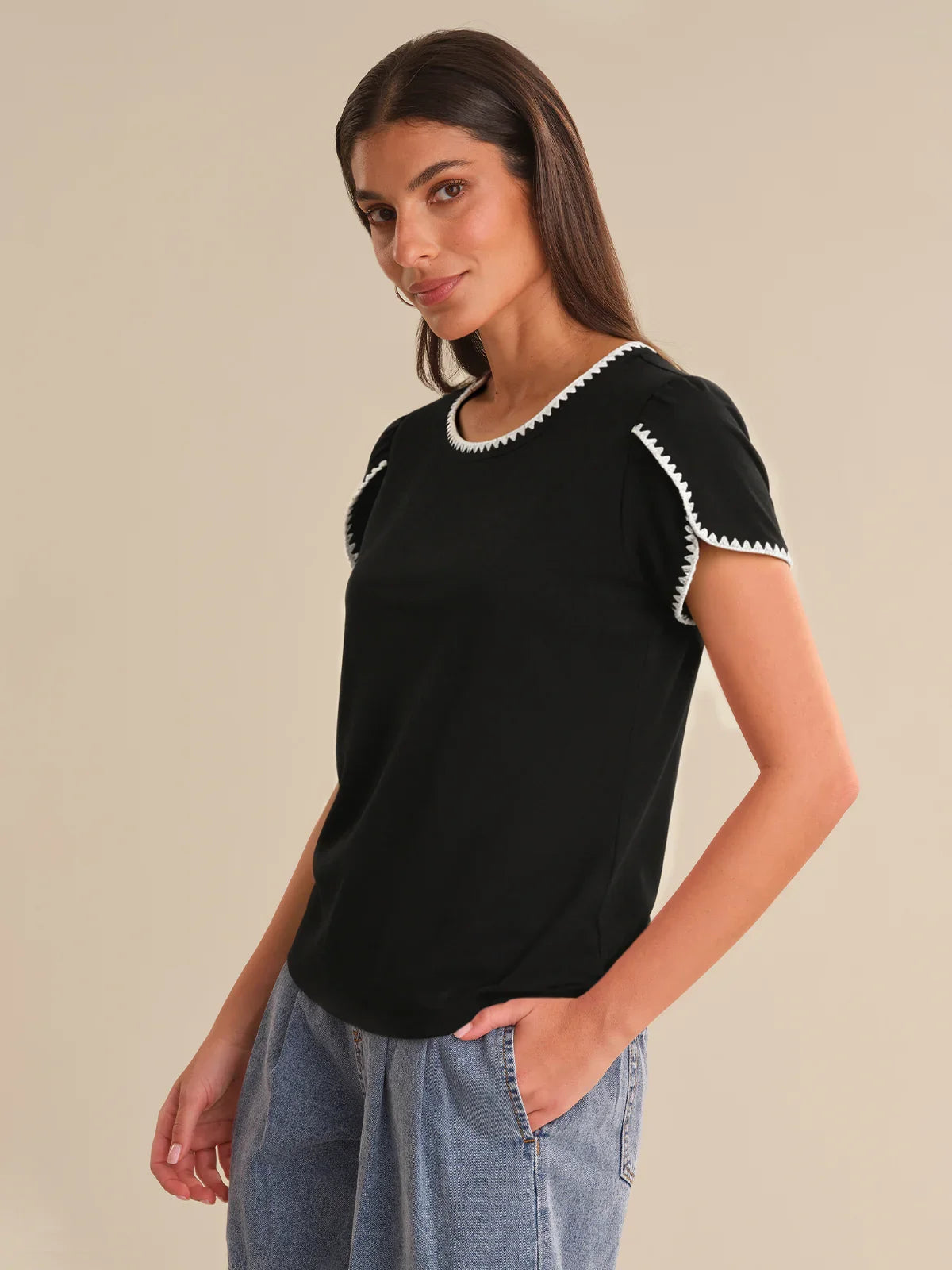 Woman wearing a black t-shirt with white trim on a beige background