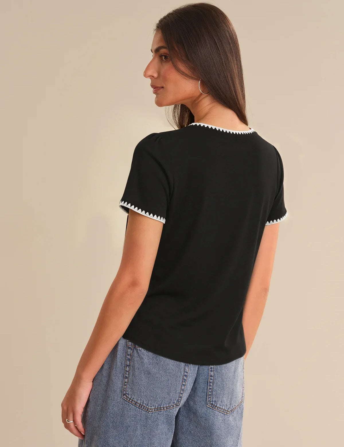 Woman wearing a black t-shirt with white trim on a beige background