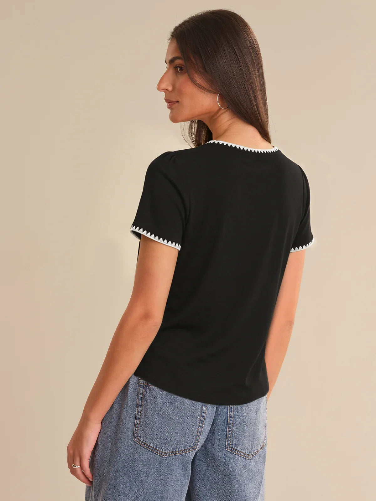 Woman wearing a black t-shirt with white trim on a beige background