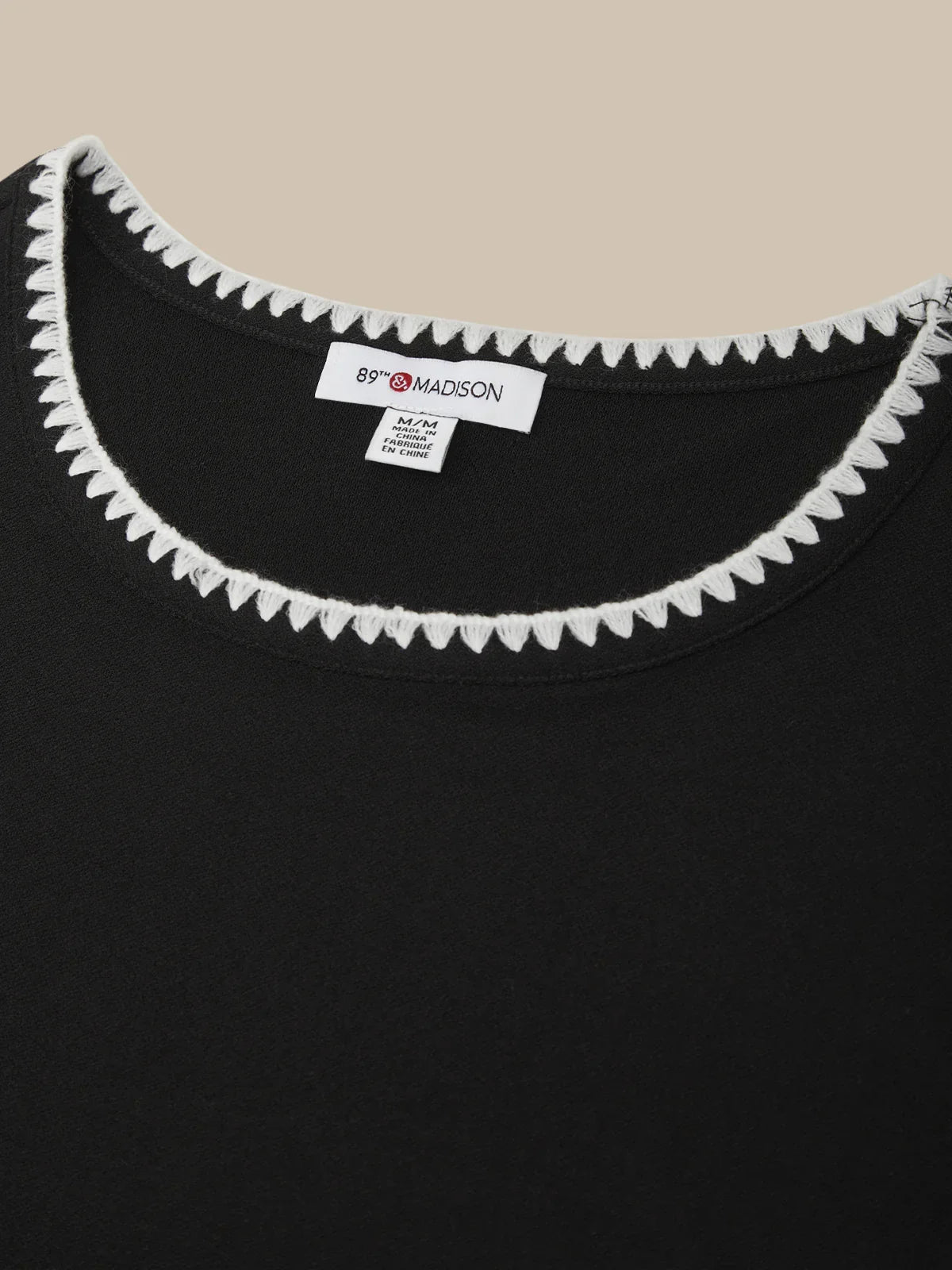 Black garment with white trim and a brand label on a beige background