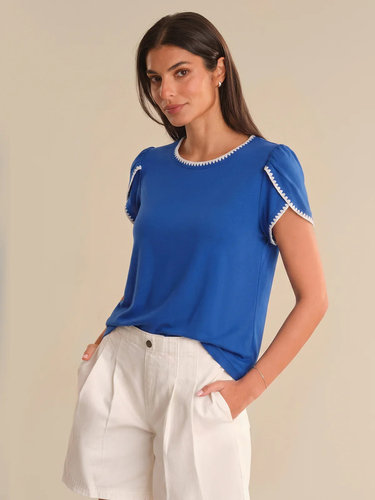 Woman wearing a blue top with white trim against a beige background