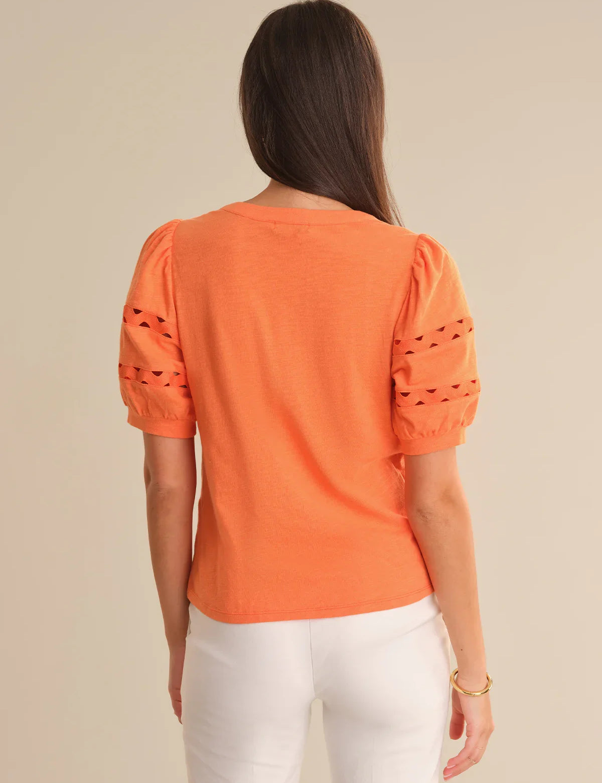 Woman wearing an orange top with cut-out sleeves on a beige background
