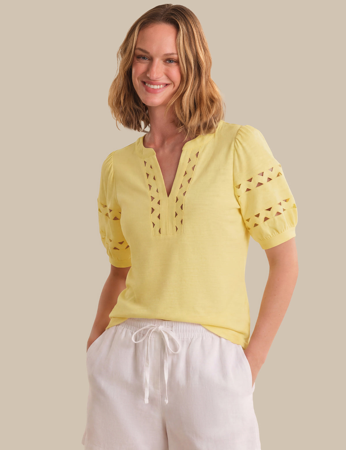Woman wearing a yellow blouse with cut-out details on a beige background