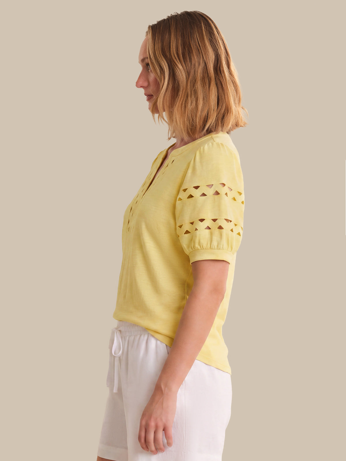Woman wearing a yellow top with cut-out sleeves against a beige background