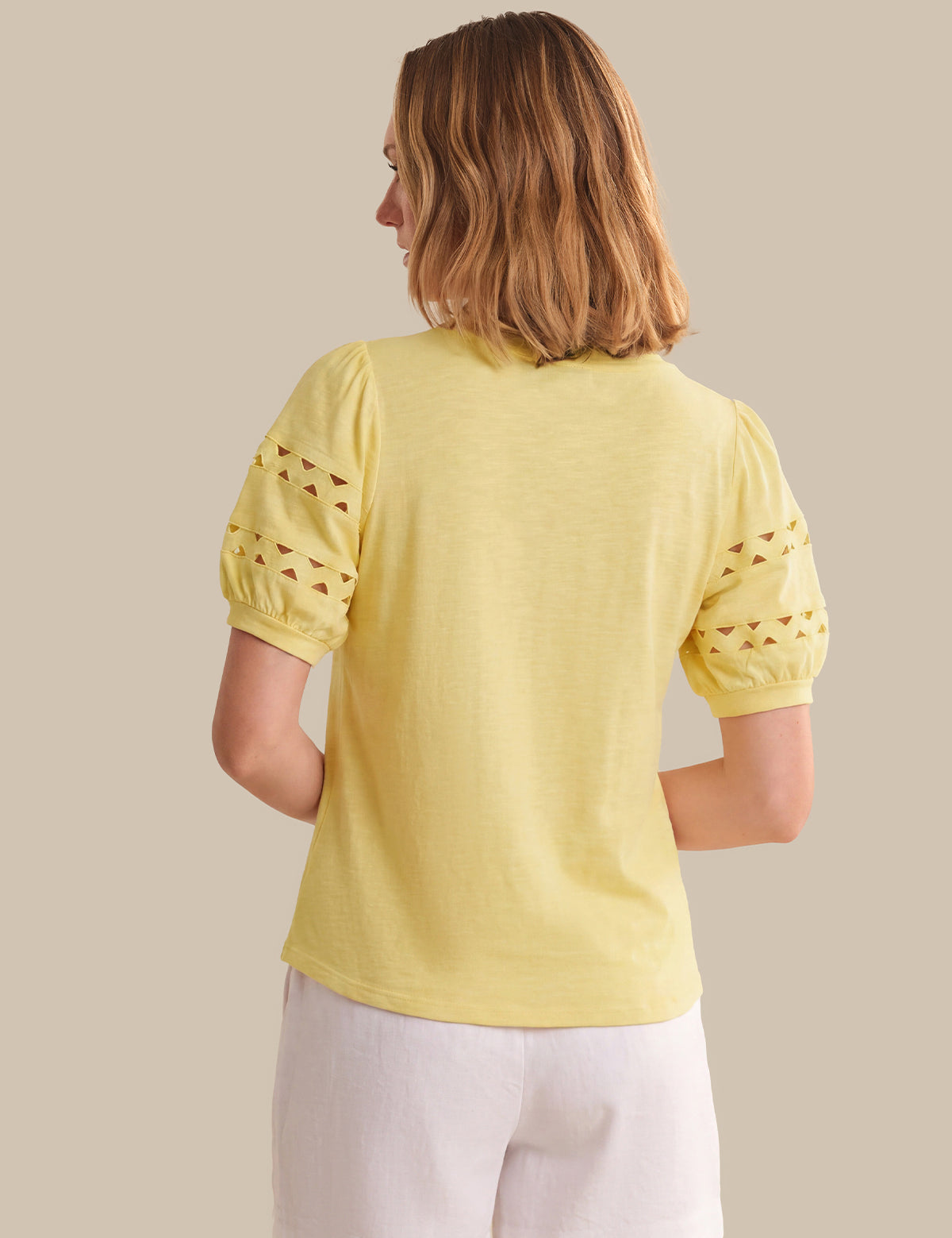 Woman wearing a yellow top with lace sleeves on a beige background