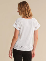 Woman wearing a white blouse with cut-out details on a beige background