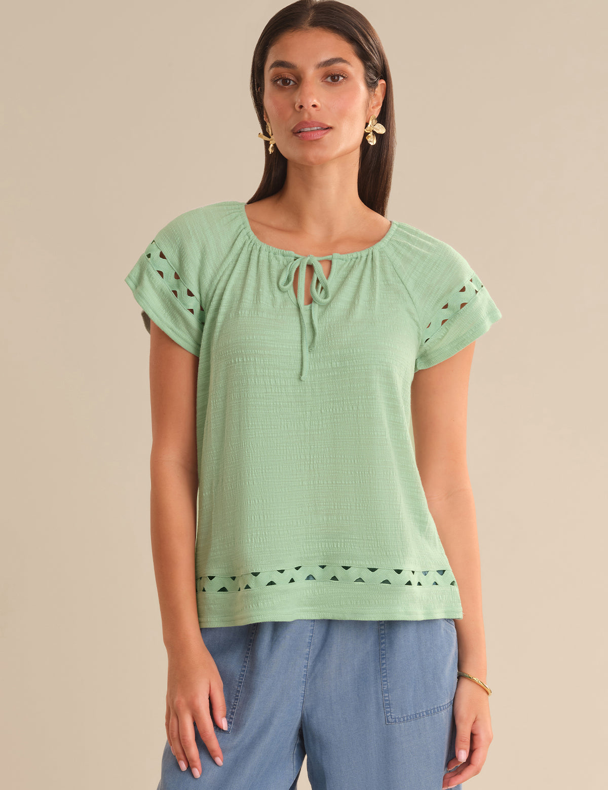 Woman wearing a light green top with lace details on a beige background
