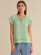 Woman wearing a light green top with lace details on a beige background