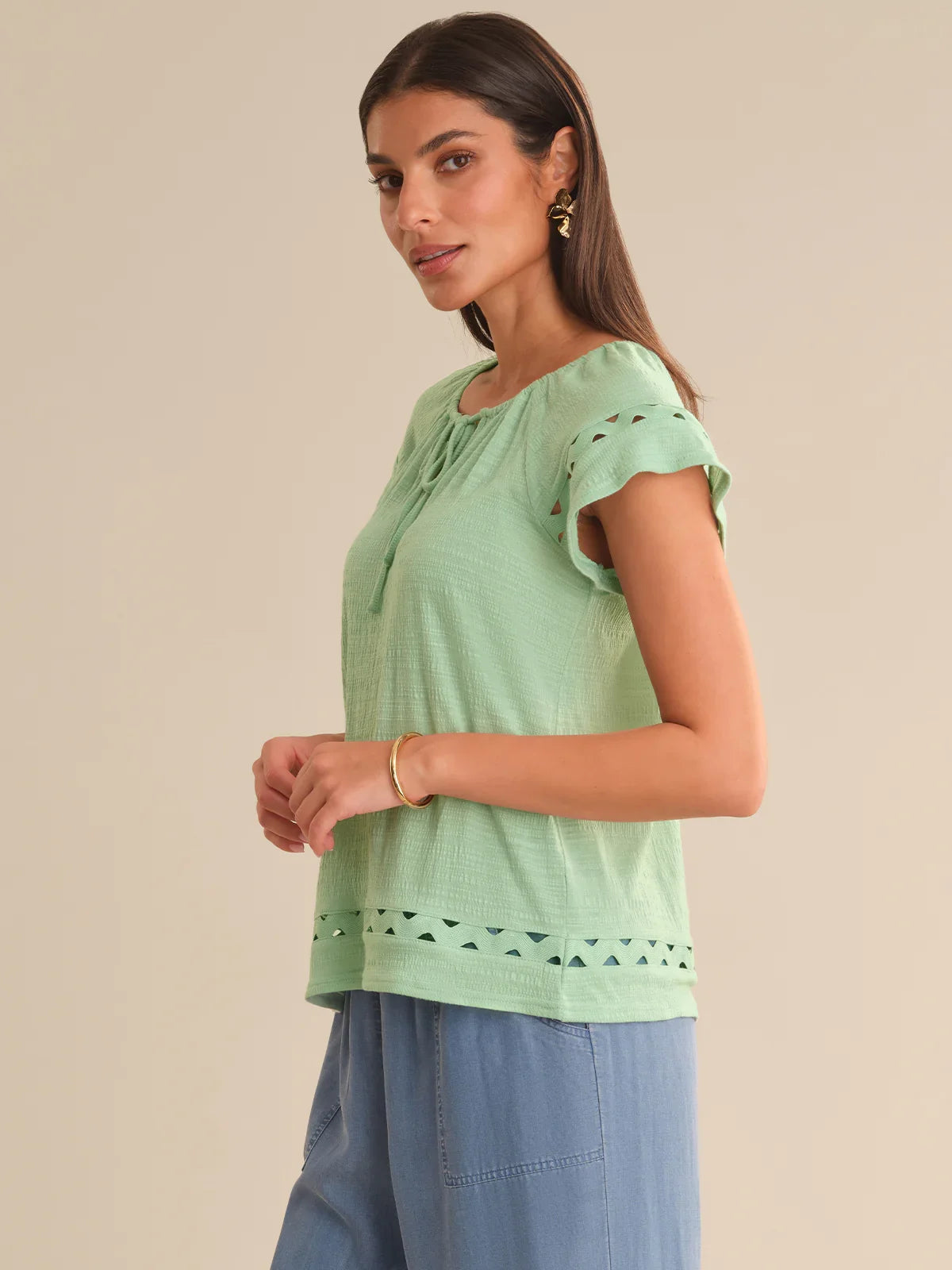 Woman wearing a light green top with lace details on a beige background