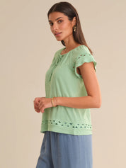 Woman wearing a light green top with lace details on a beige background