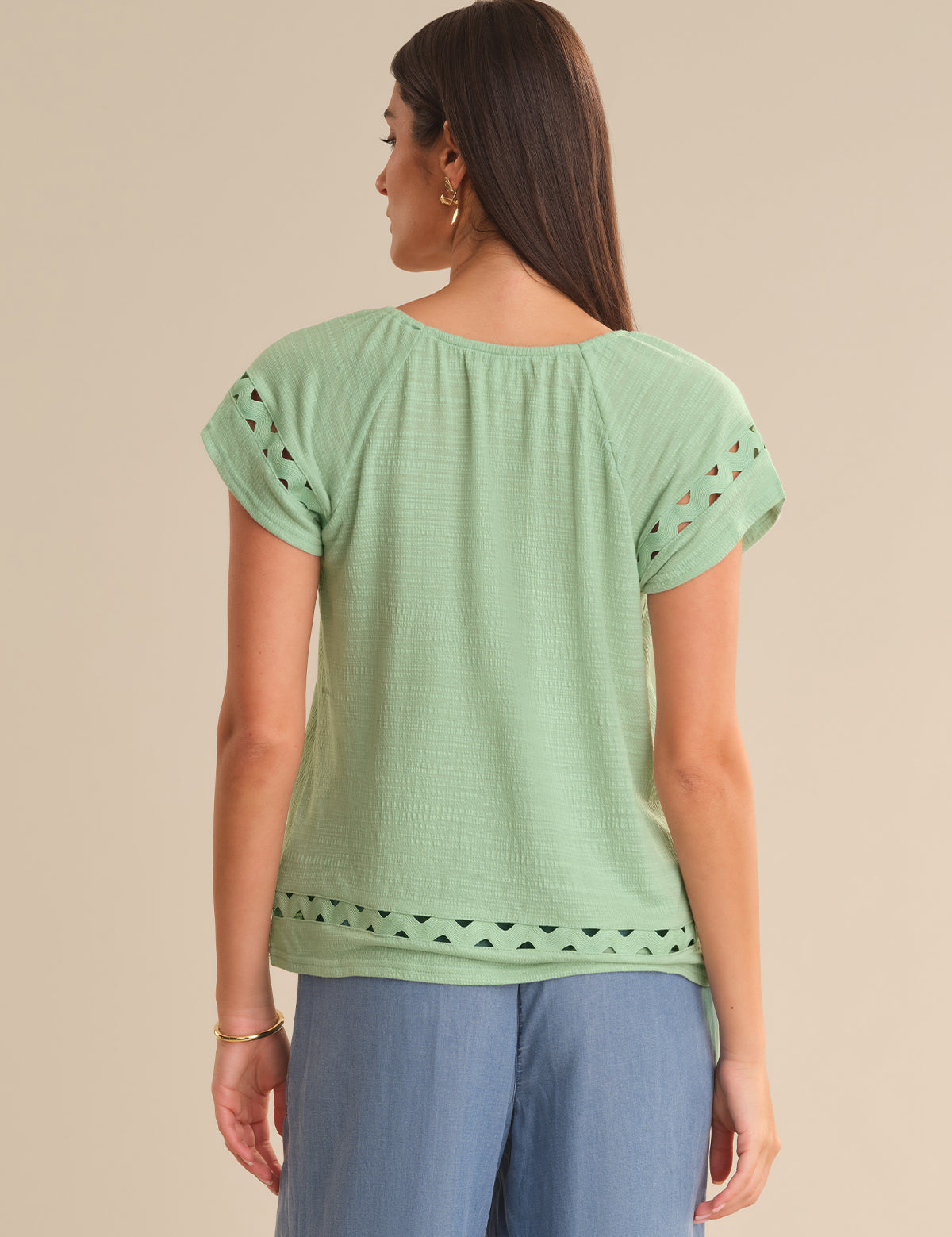 Woman wearing a green top with cut-out sleeves on a beige background