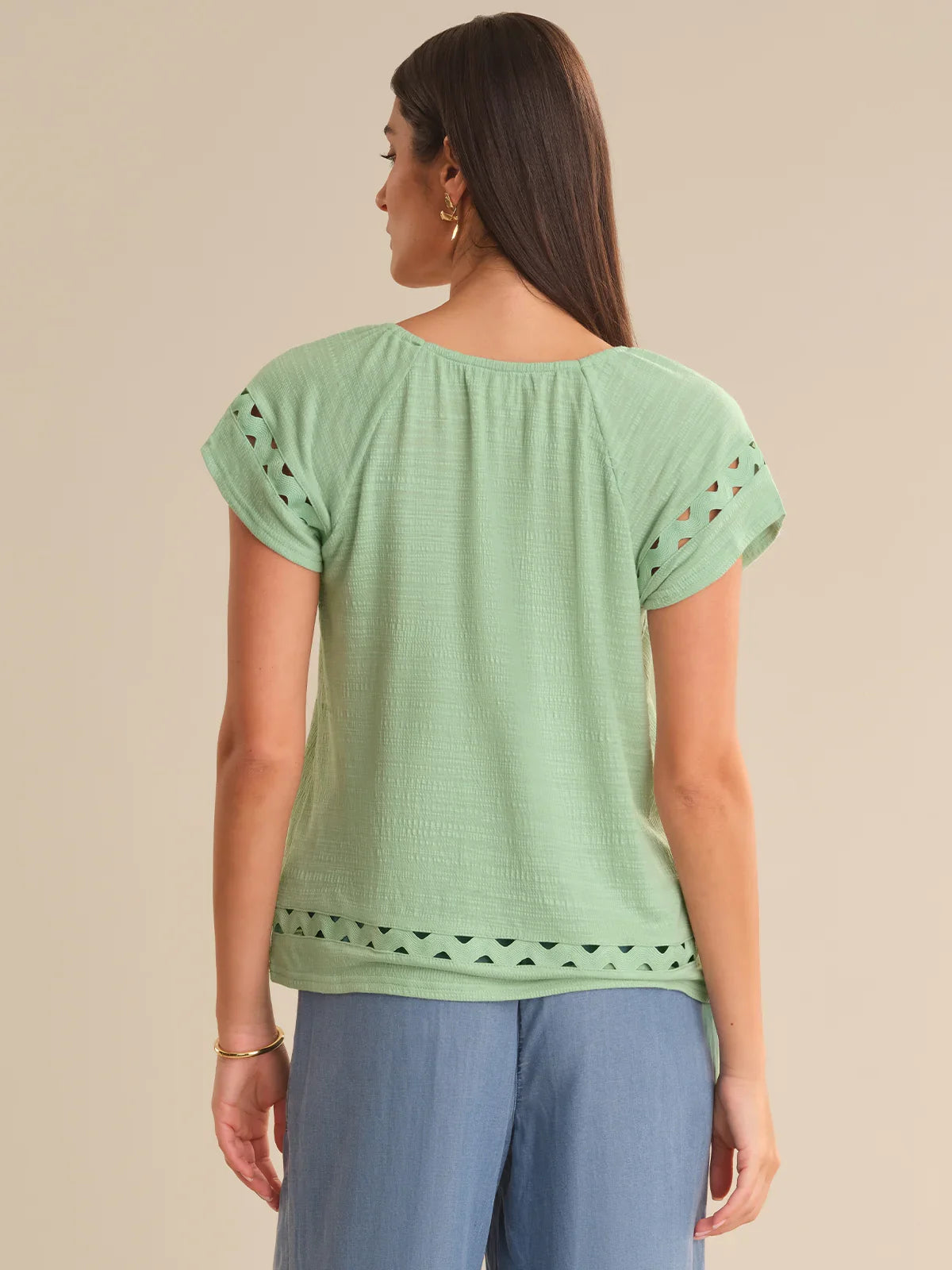 Woman wearing a green top with cut-out sleeves on a beige background