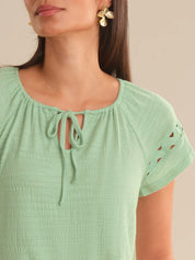 Green top with lace-up neckline and short sleeves on a neutral background