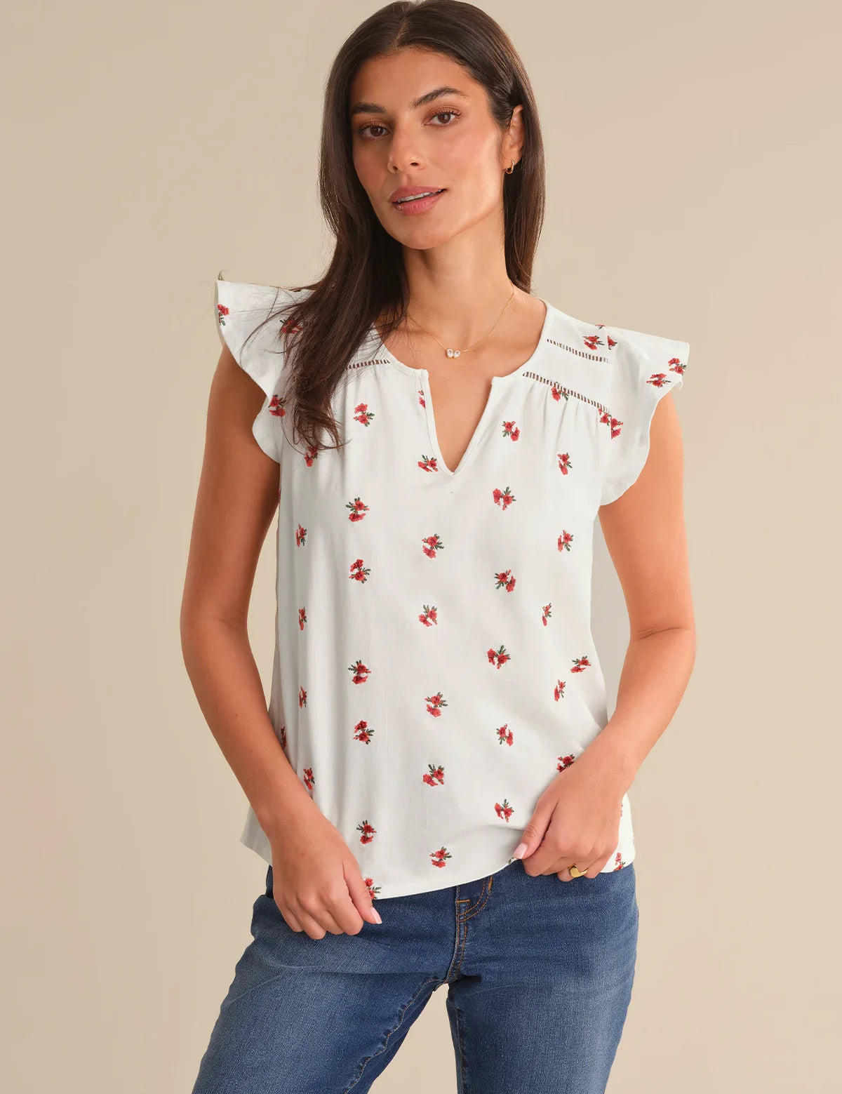 Woman wearing a white blouse with red floral patterns and blue jeans on a beige background