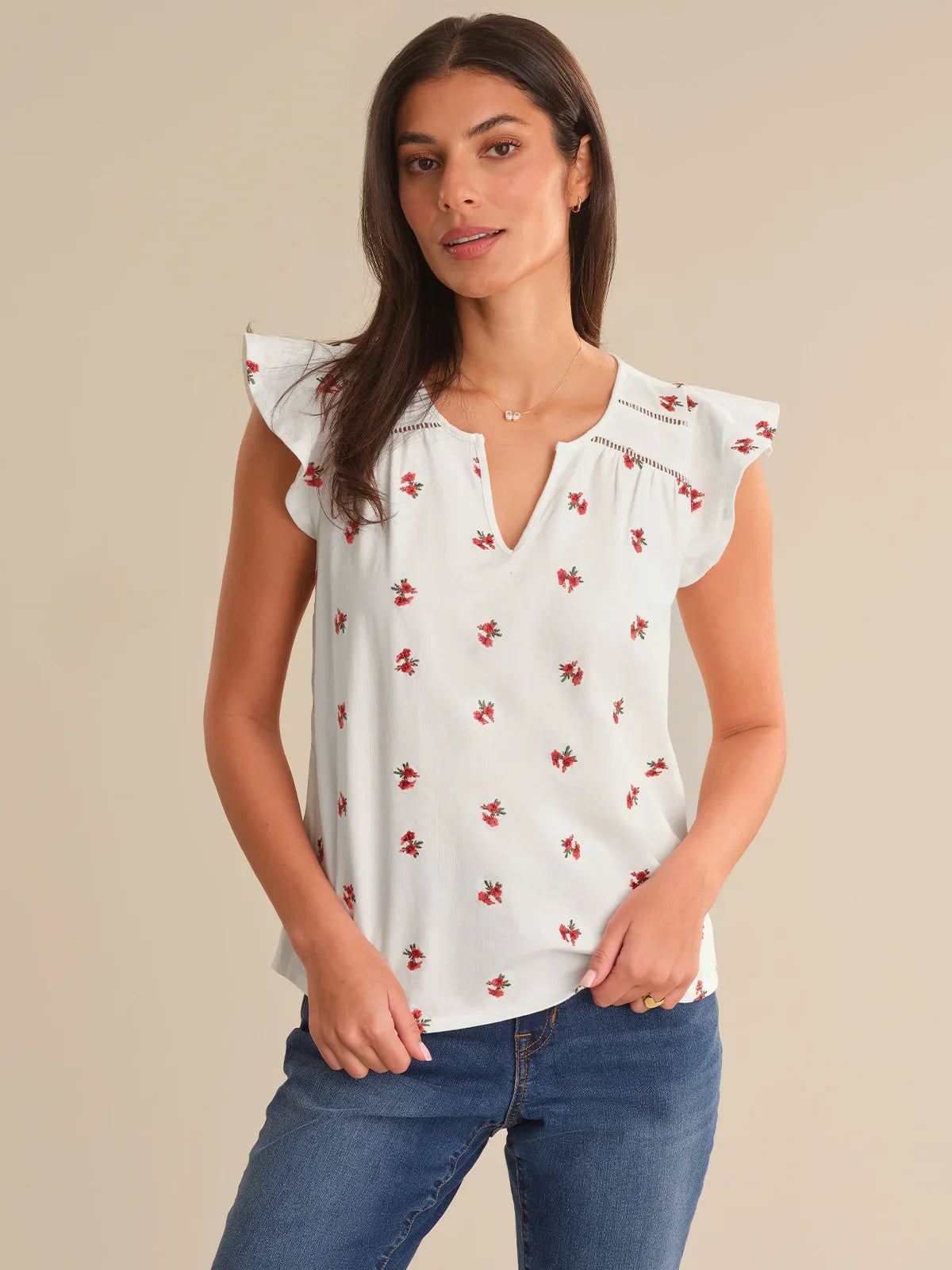 Woman wearing a white blouse with red floral patterns and blue jeans on a beige background