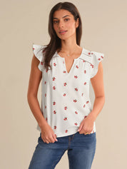 Woman wearing a white blouse with red floral patterns and blue jeans on a beige background