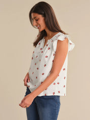 Woman wearing a white blouse with red floral patterns and blue jeans on a beige background