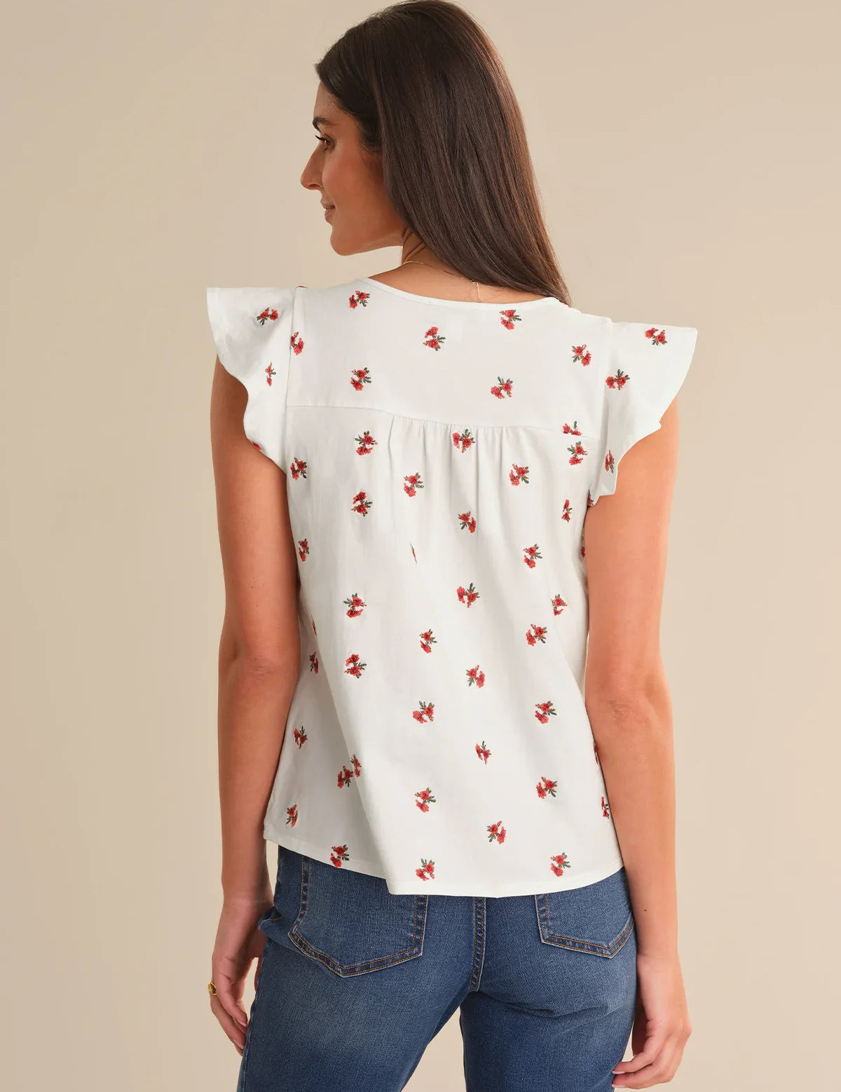 Woman wearing a white blouse with red floral patterns and blue jeans on a beige background