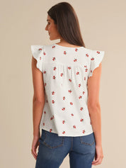 Woman wearing a white blouse with red floral patterns and blue jeans on a beige background